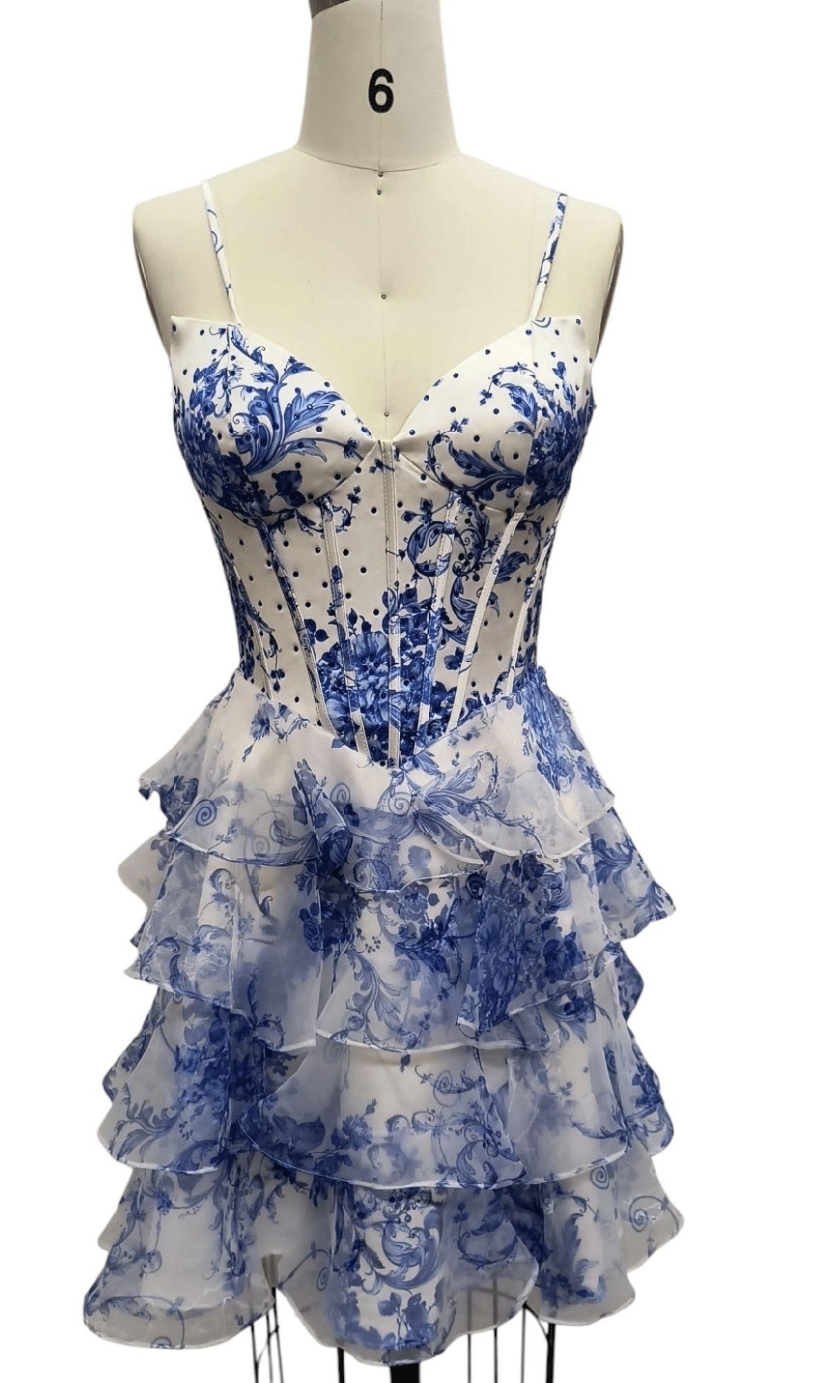 The Short Print Corset Hoco Dress: 12613 is a blue floral homecoming dress with a white base, fitted bodice with thin straps, and a layered ruffle skirt, shown on a dress form.